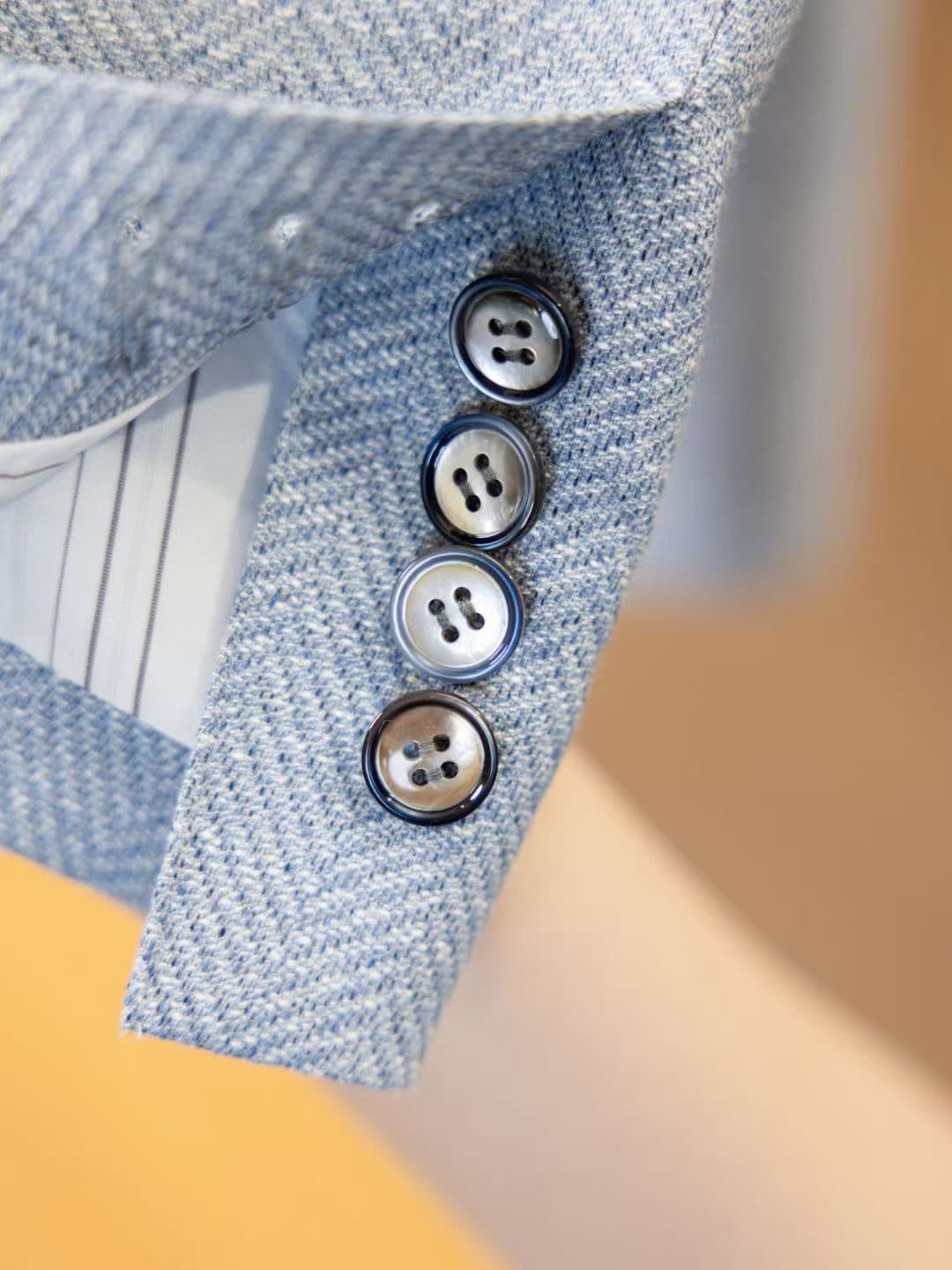 Close detail of cuff buttons and striped lining on a light-blue herringbone custom jacket