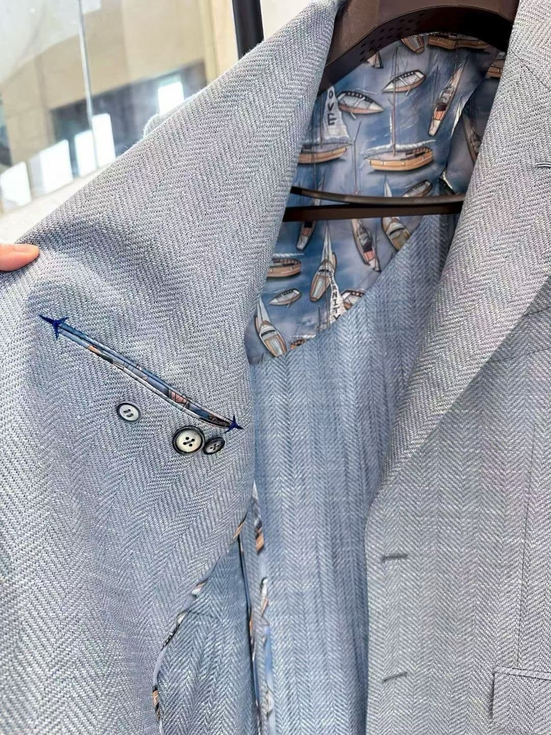 Light-blue herringbone jacket showing lapel shape, working cuff buttons, and patterned interior lining