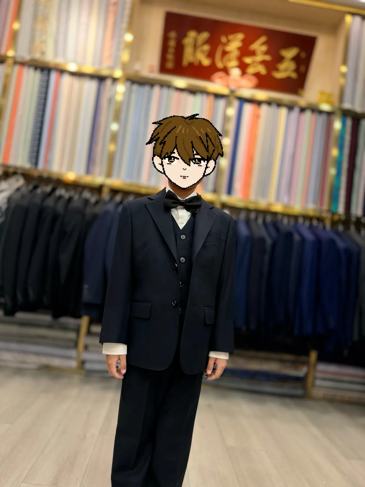 Child wearing a navy three-piece suit and black bow tie in front of fabric shelves at Wuyue