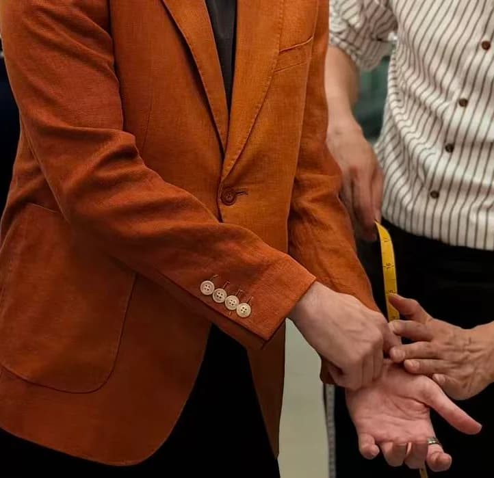 Tailor checking the sleeve and wrist position of an orange custom jacket during a Shanghai fabric market fitting