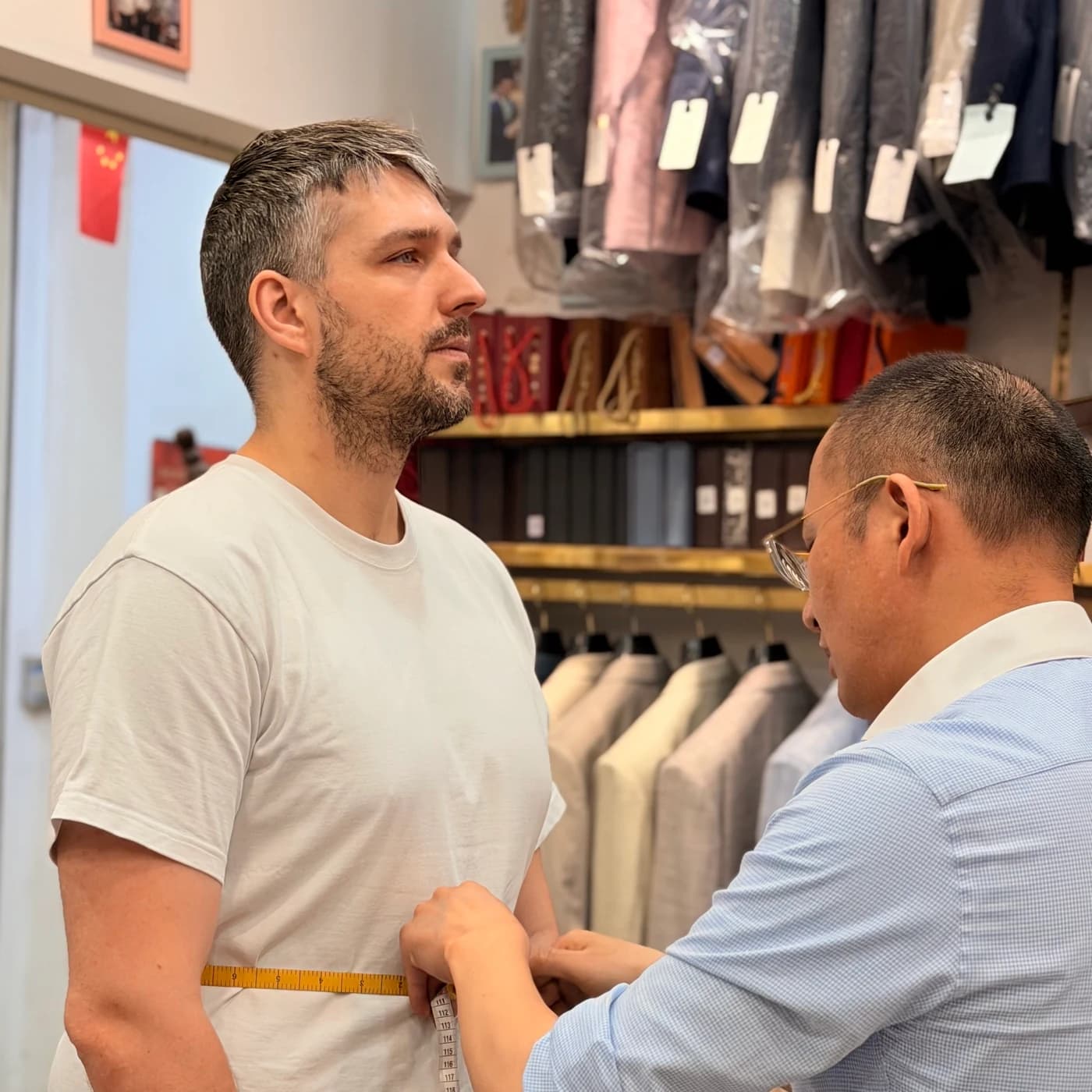 Wuyue tailor taking a client's waist measurement inside a Shanghai fabric market