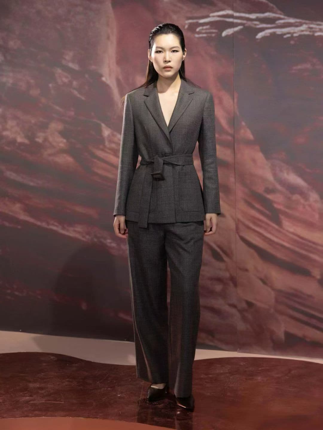 Woman wearing a grey belted pantsuit with straight-leg tailored trousers