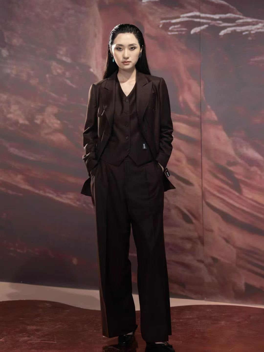 Woman wearing a dark tailored three-piece pantsuit with jacket, waistcoat, and wide-leg trousers