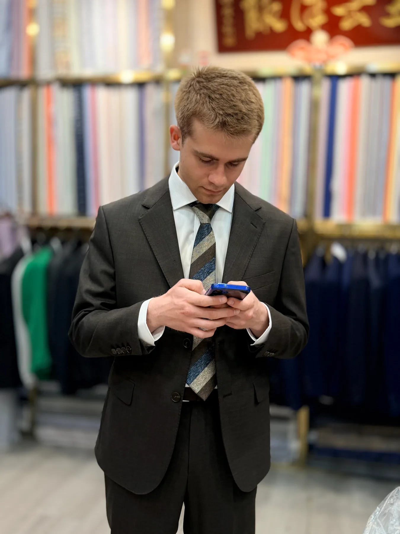 Front view of a French student looking at his phone while wearing a dark suit and striped tie