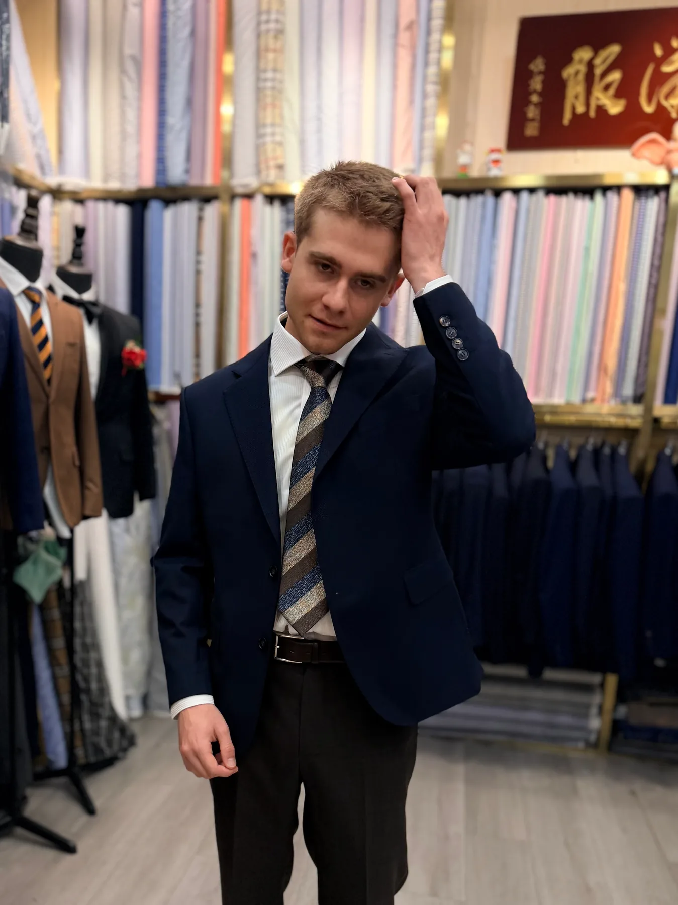 French student wearing a dark suit and striped tie with one hand raised to his hair