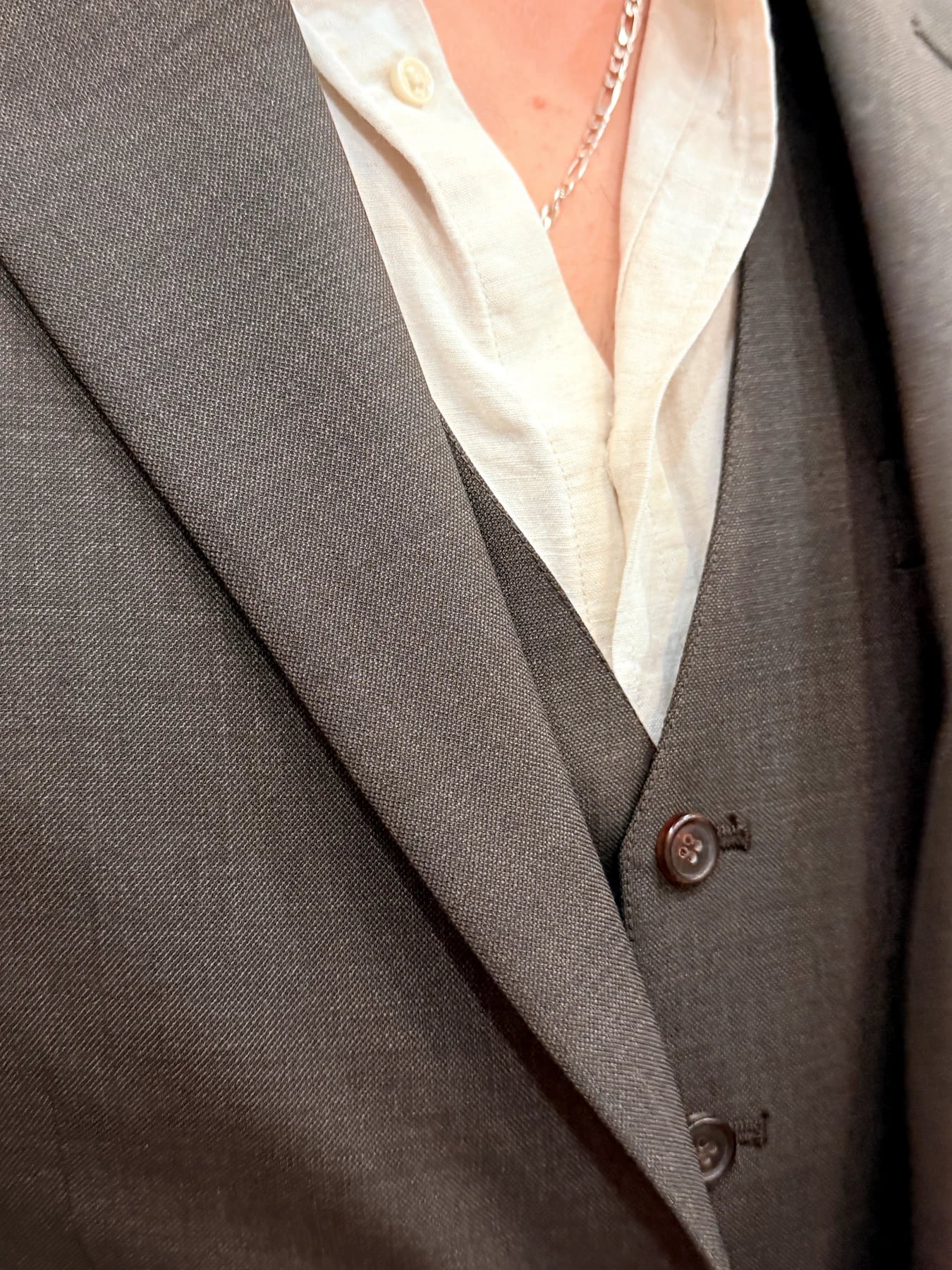 Close view of textured grey suit cloth, notch lapel, waistcoat, and brown buttons