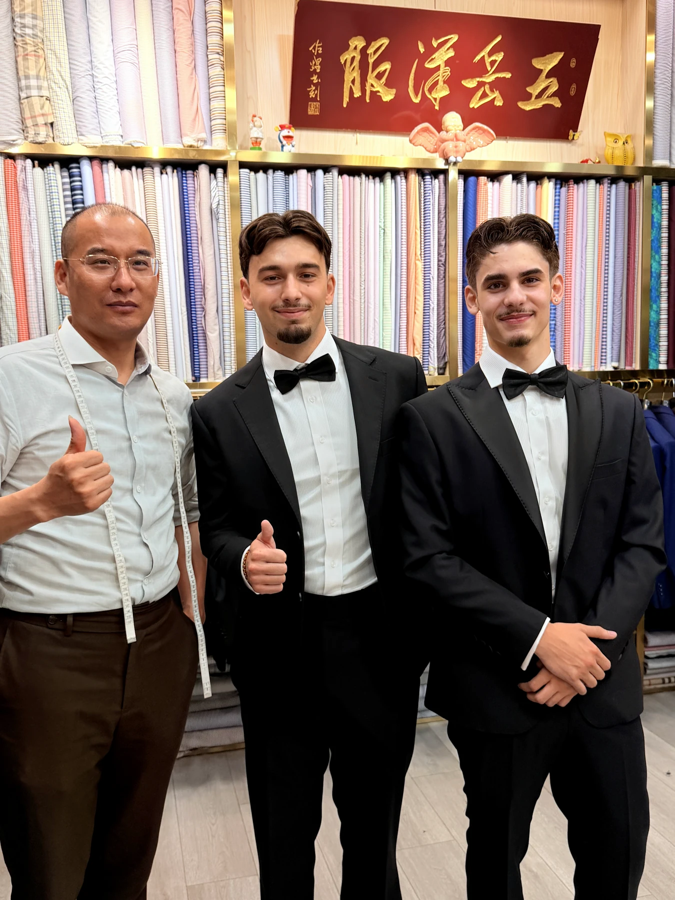 Wuyue tailor standing with two clients in finished black tuxedos inside the shop
