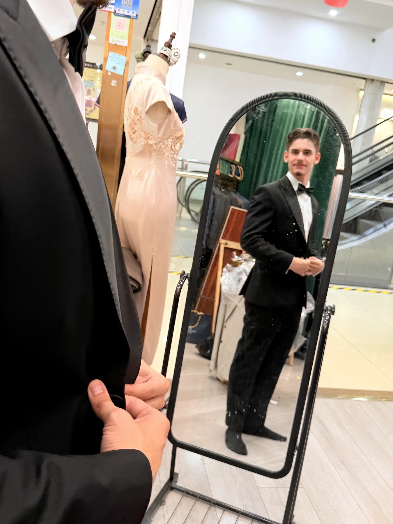 Client checking the front of a black tuxedo in a full-length mirror at Wuyue